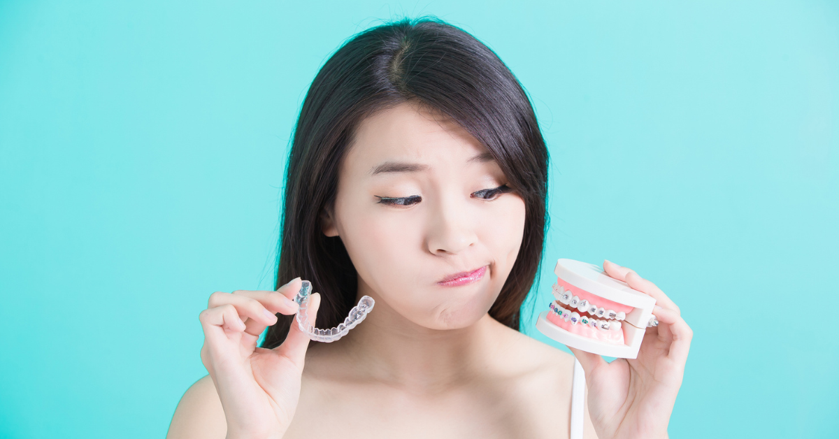 Aligners vs Braces - A woman with long dark hair looks puzzled while holding a clear dental aligner in one hand and a dental model with braces in the other, set against a teal background.